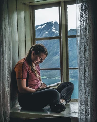 A vertical shot of a caucasian female sitting on a windowsill and reading