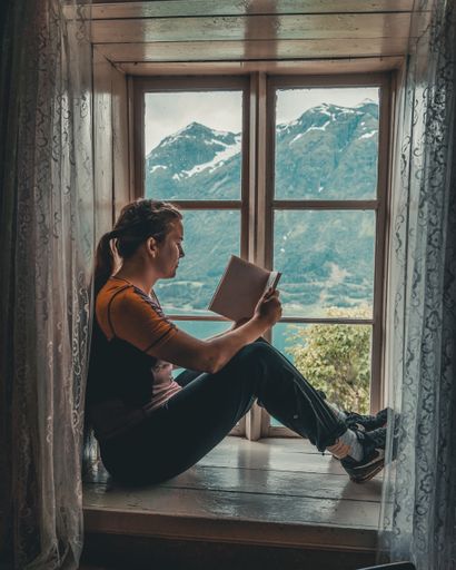 A side view of a female reading book by the window