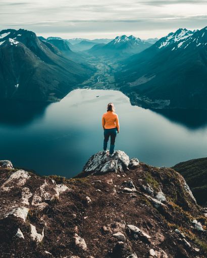 A vertical shot of a woman standing on the edge of a mountain por to enjoy the scenery of the lake