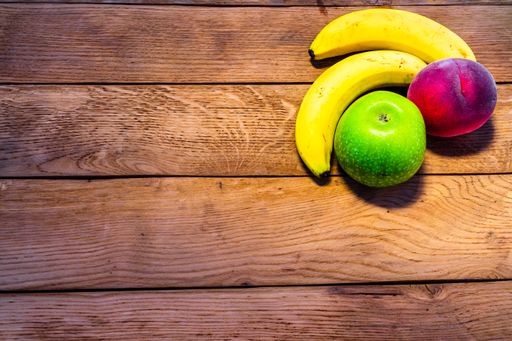 A top view of a mix of fruits on a wooden table - banana, apple, nectarine
