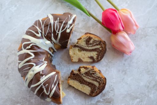 A top view shot of slices of zebra bundt cake and pink tulips on a white marble background