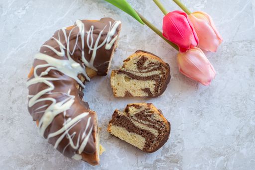 A top view shot of slices of zebra bundt cake and pink tulips on a white marble background