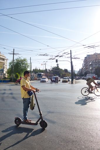 A vertical shot of people moving by different vehicles on a sunny day in Athens, Greece