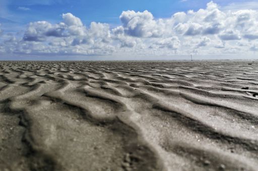 A low angle shot of the patterns on the wet sands on the beach under the beautiful cloudy sky