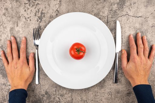 A photo of man's hands holding fork and knife and a tomato on a plate