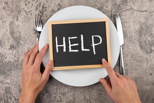 A photo of man's hands with fork, knife and a "help" word on a board on a plate