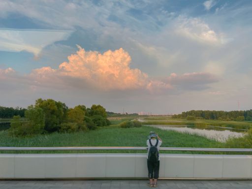 A photo of a man standing next to an outdoor railing and watching the sunset glow