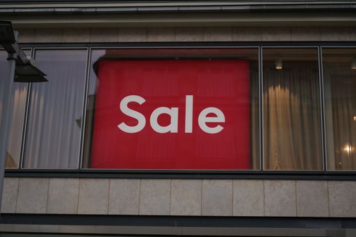 A closeup shot of a red sign with "Sale" written in white letters on a window of a store