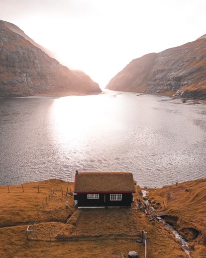 A vertical shot of a small hut on a lakeshore with mountains in the background