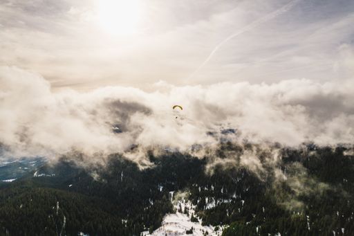 The paraglider floating against the white clouds above the green hills.