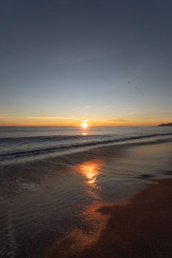 A vertical shot of seashore with the sun reflecting in the water during sunset