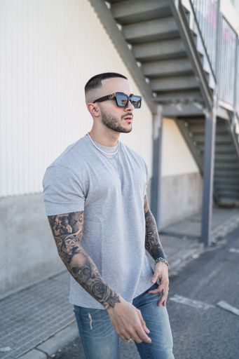 A portrait of a handsome Spanish man with tattoos wearing a gray t-shirt with sunglasses