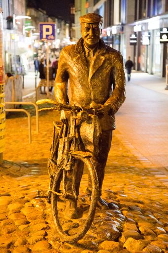 A vertical shot of an old man with bicycle statue along the street