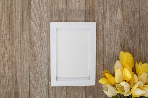 A closeup of the blank paper with white frame on the wooden surface with a bouquet.