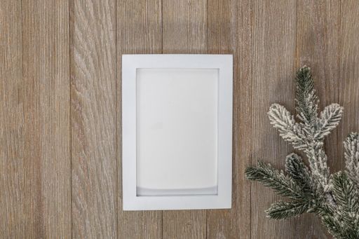 A closeup of the blank paper with white frame on the wooden surface with a spruce branch.