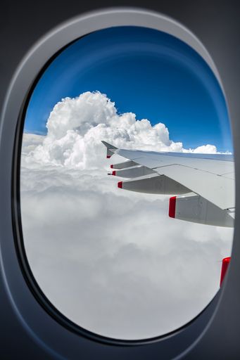 A vertical shot of fluffy clouds in blue sky seen from an airplane window