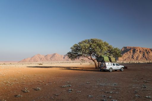 An off-road vehicle with roof tent on a sandy track in the sunset in the Naukluft Mountains in Namibia