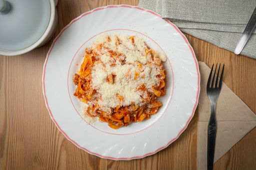 A top view of a plate of delicious pasta with meat, sauce, and grated cheese on the table