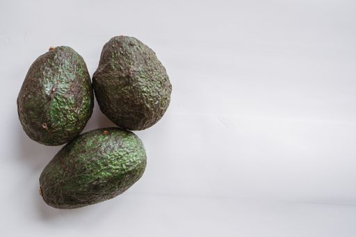 A high angle shot of three ripe avocados under the lights isolated on a grey background