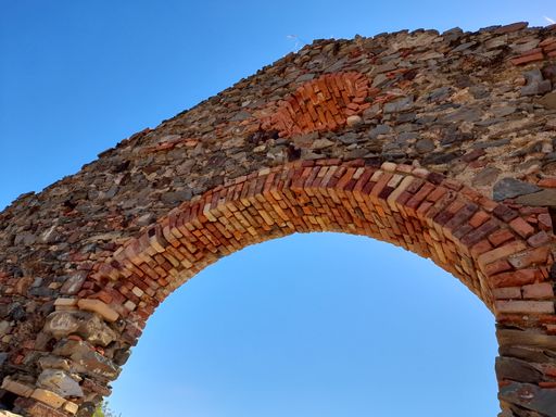 A bottom shot of an ancient arch in the background of blue sky.