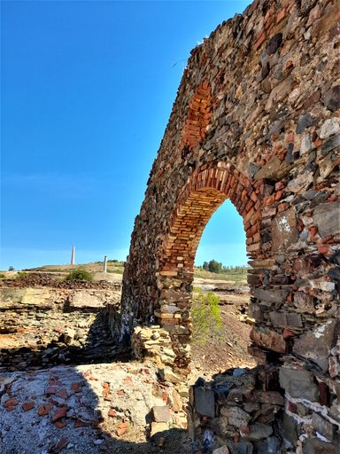 A vertical shot of an ancient arch entrance in the background of blue sky.
