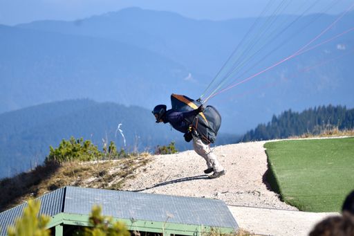 A closeup of a man jumping with a parachute from the edge of a hill