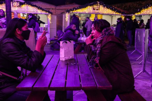 Two ladies at an open air table, relaxing after shopping. One conversing on her mobile, the other masked because of Covid, playing with her mobile