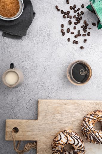 A vertical top view of a glass of coffee and milk on a kitchen table with donuts