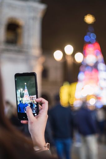A shallow focus of a woman taking pictures of a Christmas tree with her smartphone
