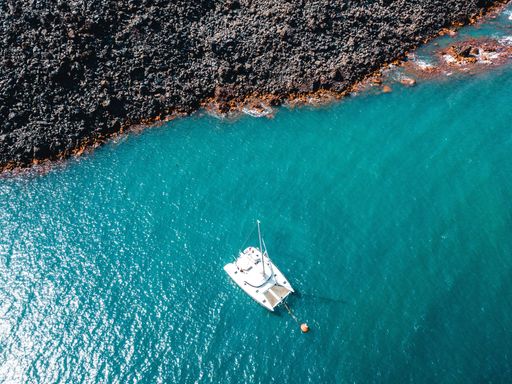 An aerial shot of a white sailing boat in the turquoise sea