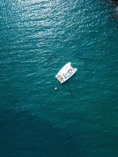 A vertical aerial shot of a white sailing boat in the turquoise sea