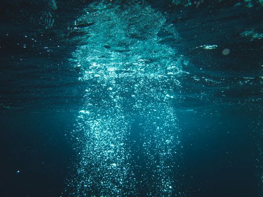 An underwater shot of sun rays going through deep ocean making water bubbles