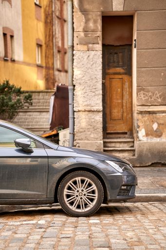 Side of a parked car next to a sidewalk and an old building in the Tumski island.ca