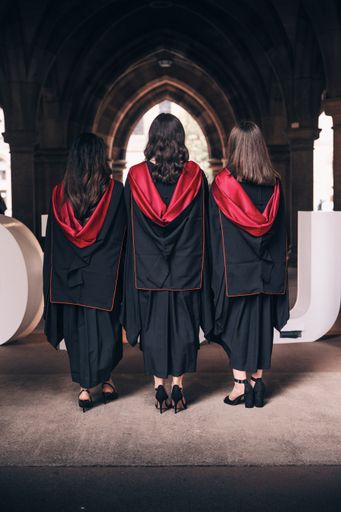 A vertical shot of three university graduates in their graduation gowns from behind