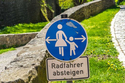 A dirty road sign of mother and child for Cyclist Dismount in German language on a sunny day