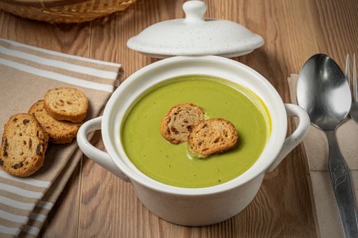 A closeup of a bowl of delicious green pea puree soup with croutons on the table
