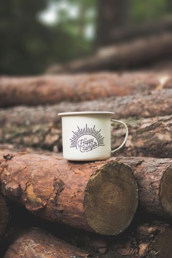 A vertical shot of a metallic cup with a [Happy camper] text written on it on trees in a forest