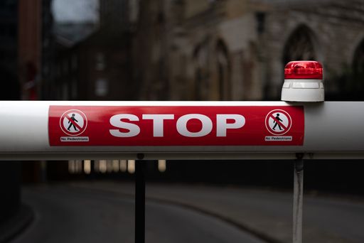 A close-up shot of a stop sign on a vehicle barrier at the entrance to a car park, with "no pedestrians" written on it also