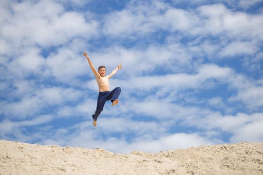 A lonely Caucasian child doing parkour on the sand.