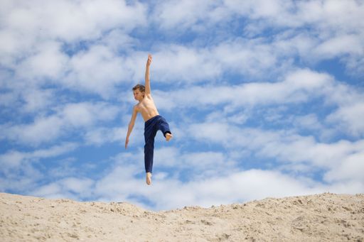 A lonely Caucasian child doing parkour on the sand.
