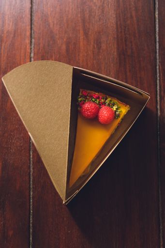A top view of a mango cheesecake with raspberries in a cake box