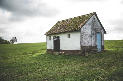A brown and white wooden shed on field of grass under the beautiful cloudy sky at daytime