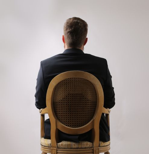 A male sitting on a chair looking at the wall taken from behind - depression concept