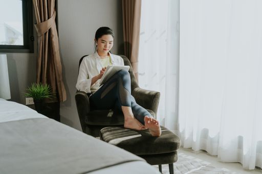 A Southeast Asian female sitting on an armchair and looking at her tablet with a wireless earphone