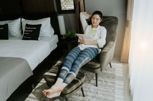 A Southeast Asian female sitting on an armchair and looking at her tablet with a wireless earphone