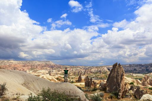 A young Caucasian man stands on top of a hill and looks up at a cloudy blue sky in Cappadocia.