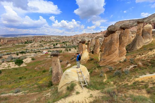 A young man with a backpack is standing on top of a rock in Cappadocia with his arms spread out on mountains
