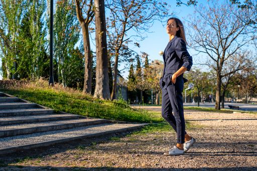 The young woman in a navy blue suit and white t-shirt with hands in pockets in the park.