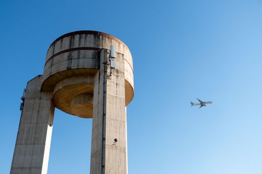 The airplane in the sky with a water tank made of concrete in the foreground.