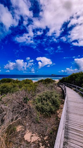 A wooden footpath leading to a beautiful sandy beach under a blue cloudy sky on a sunny day